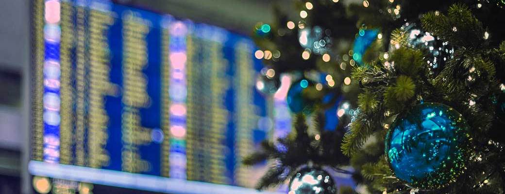 Detalle de un árbol de Navidad decorado en tonos azules en frente de una pantalla de aeropuerto.