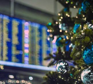 Detalle de un árbol de Navidad decorado en tonos azules en frente de una pantalla de aeropuerto.